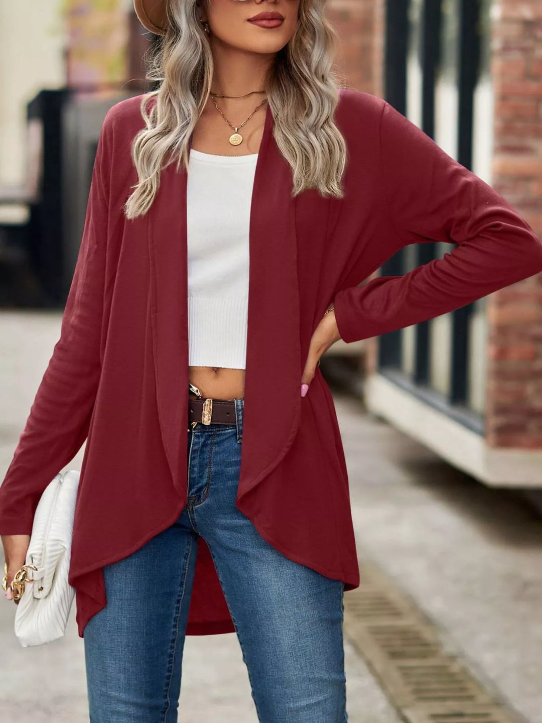 Burgundy cardigan in a hand on hip pose with a white clutch
