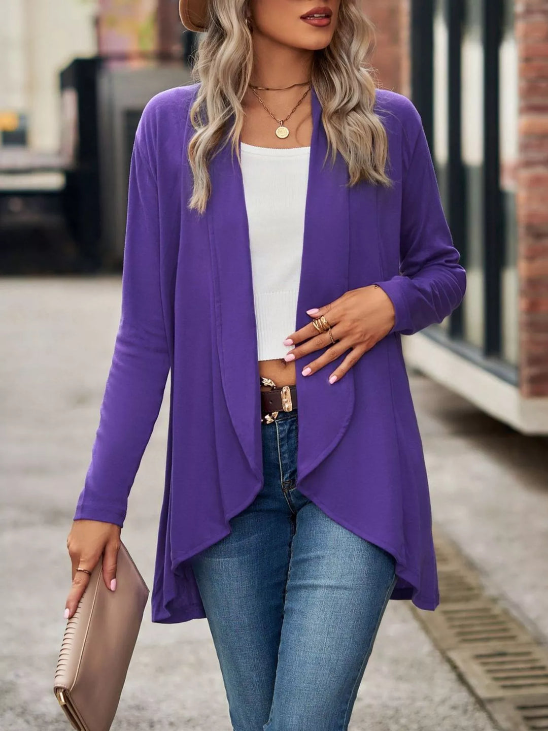Purple long waterfall cardigan worn open, holding a nude clutch bag