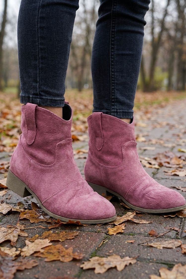 Women's dusty pink cowgirl booties worn with jeans in fall leaves