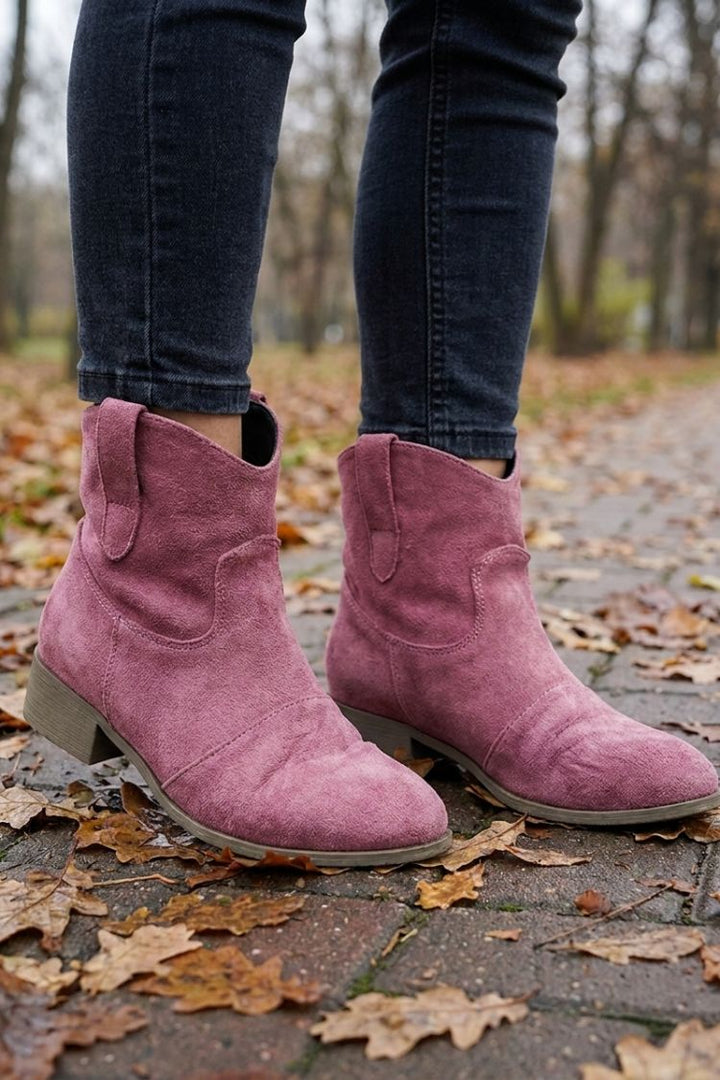 Women's dusty pink cowgirl booties worn with jeans in fall leaves