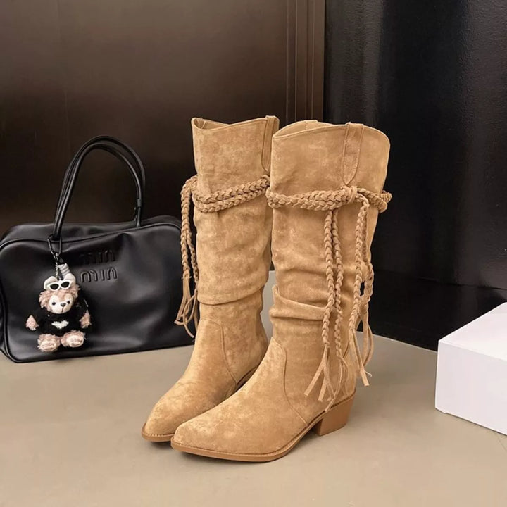 Pair of camel fringe western boots standing next to a black handbag