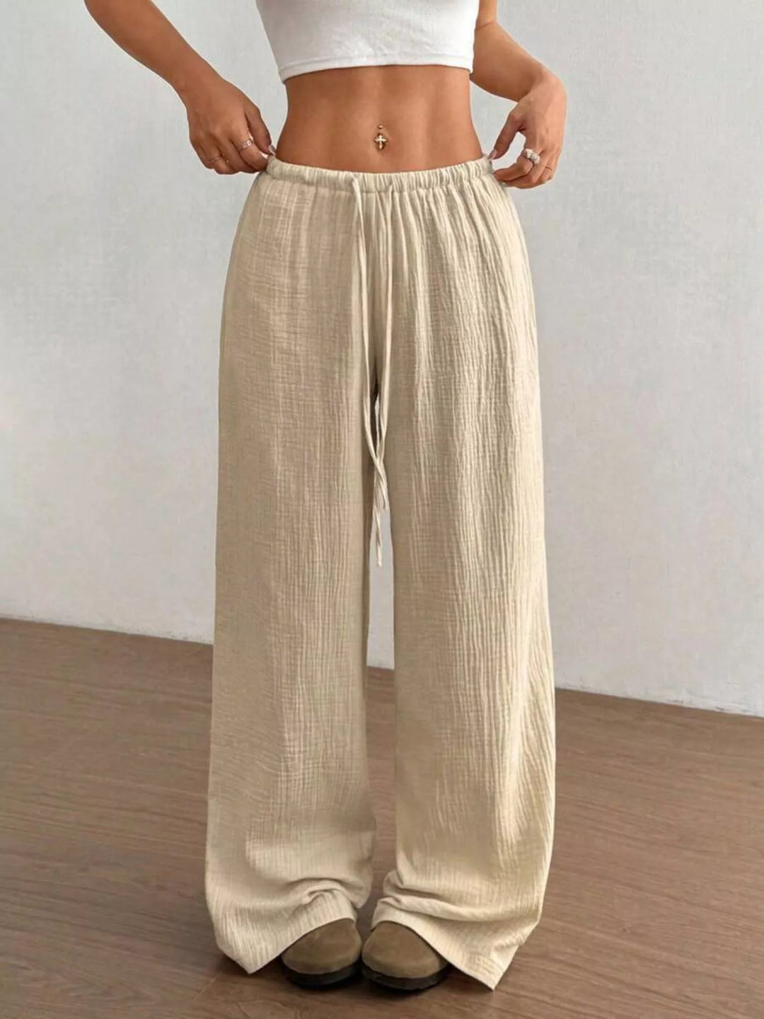 Beige crinkled wide leg pants worn with hands on the waistband
