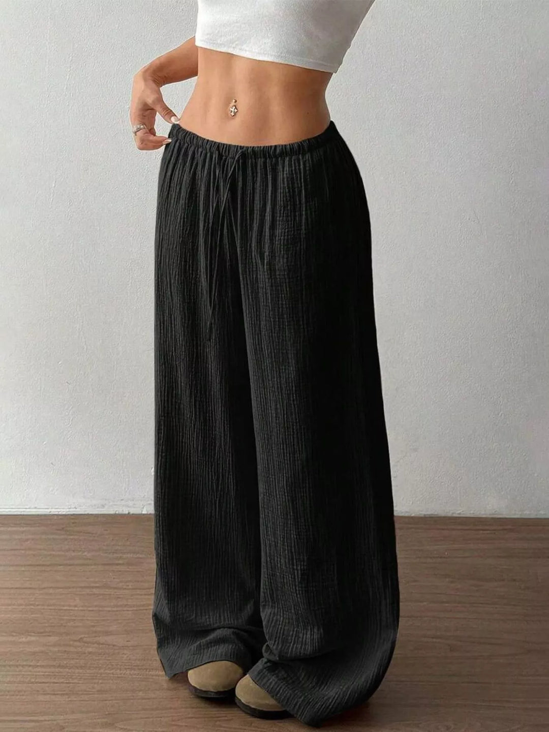 Black crinkled wide leg pants, hands on waistband, front angle