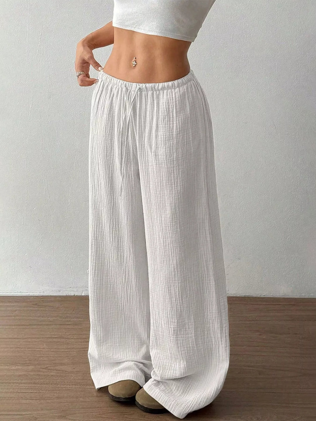 Close front view of the white drawstring wide leg pants on a wood floor