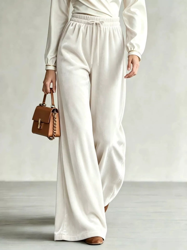 Ivory drawstring wide leg pants with velvet-look finish, walking with a tan bag