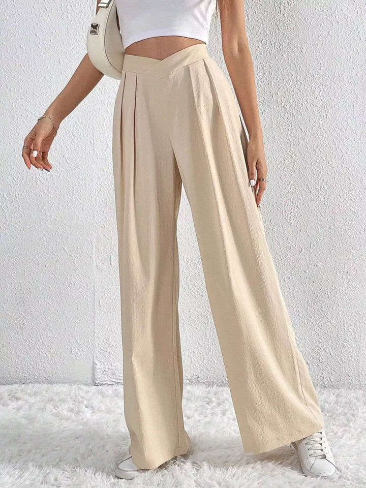 Women's beige wide leg pants with high waist and pleats, front view with sneakers