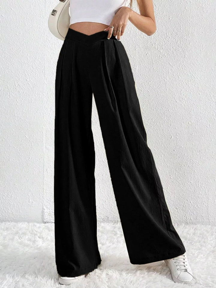 Black pleated wide leg pants, angled view with a shoulder bag