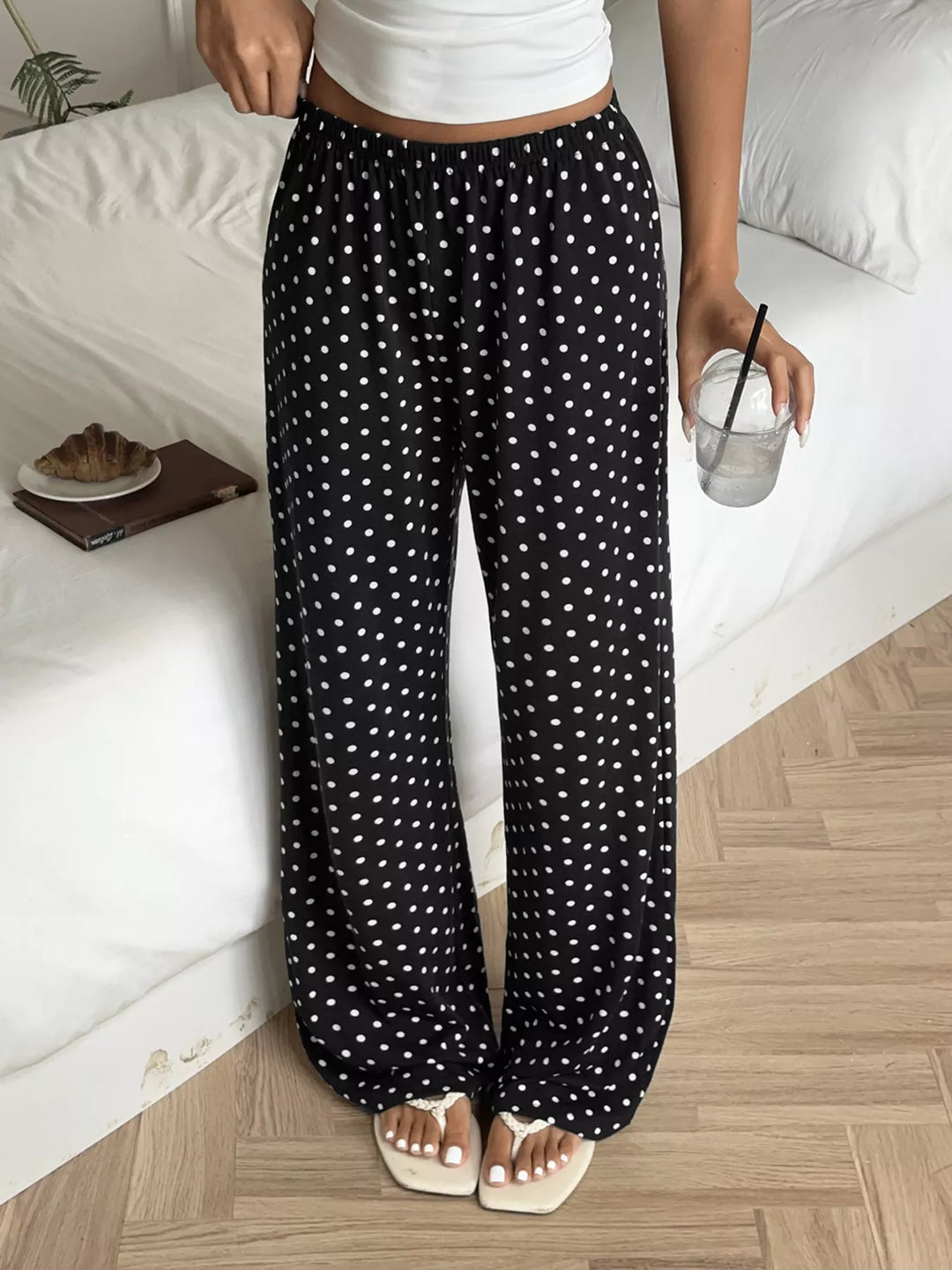 Black polka dot flowy leg pants worn with a white crop top, holding a drink