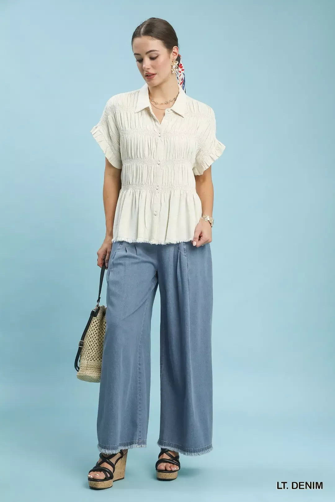 Full-length view of the light denim pleated pants styled with a cream blouse and straw bag
