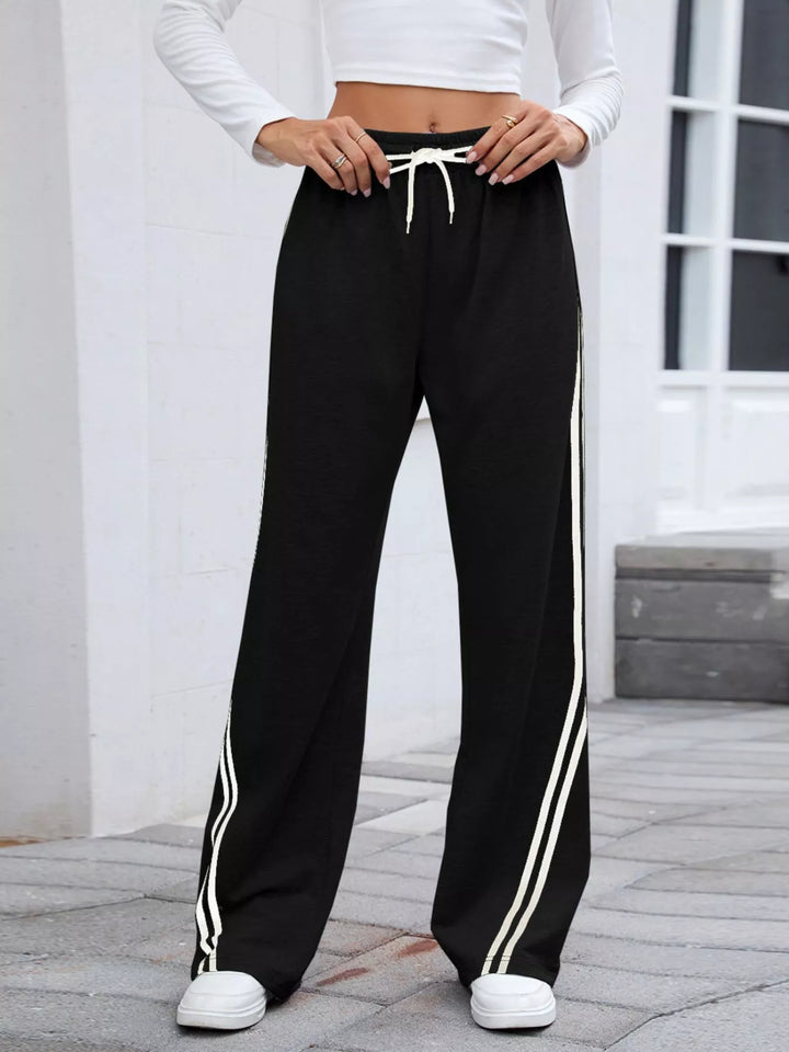 Black high rise drawstring pants with white side stripes, straight on front view