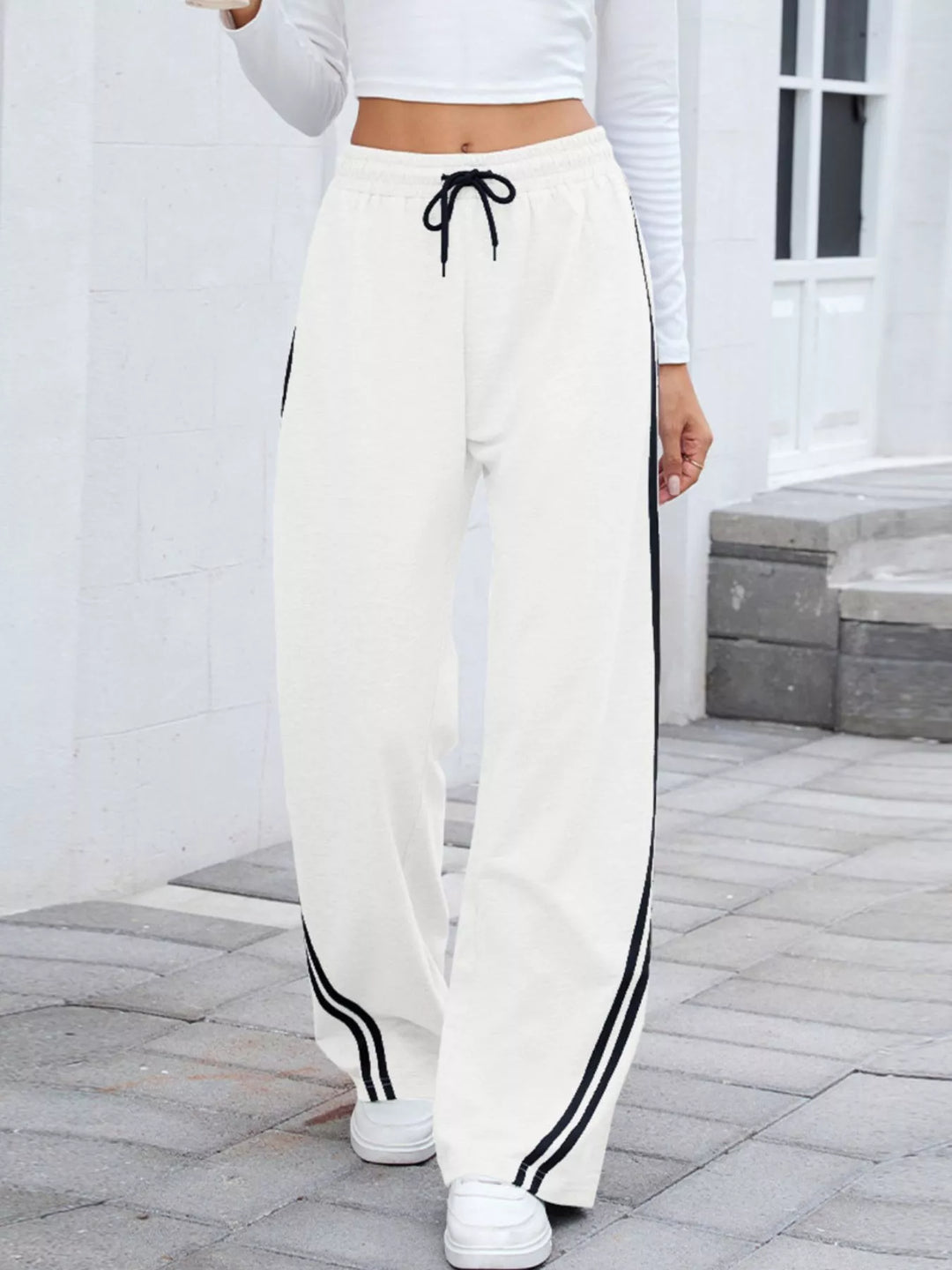 White wide leg pants with black side stripes and drawstring waist, front view