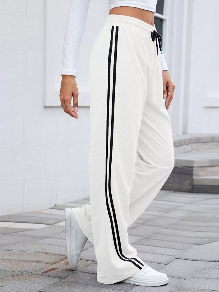 White wide leg pants with black stripes, side view in white sneakers