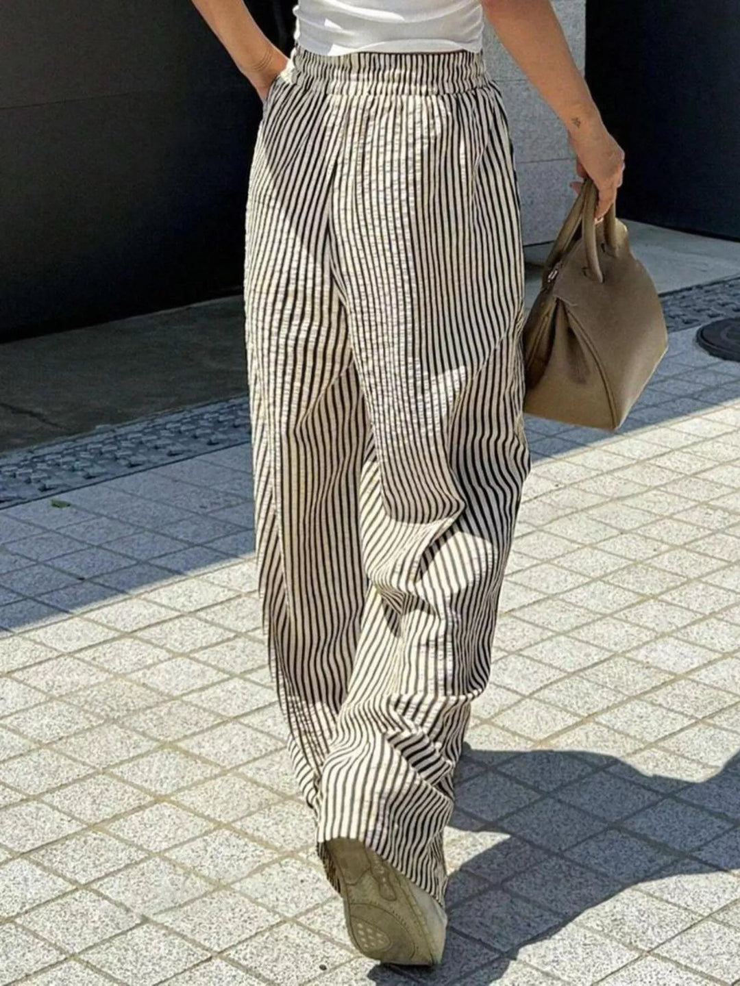 Taupe striped wide leg pants walking with a tan bag