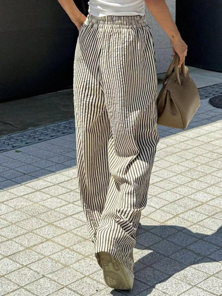 Taupe striped wide leg pants walking with a tan bag