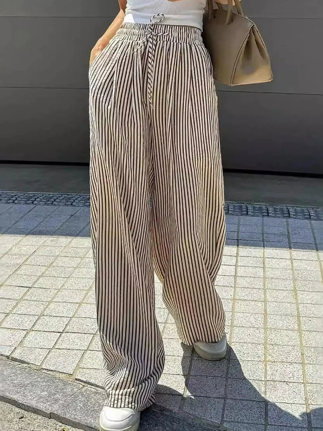 Taupe pinstripe pants with a hand in pocket, outdoor street view