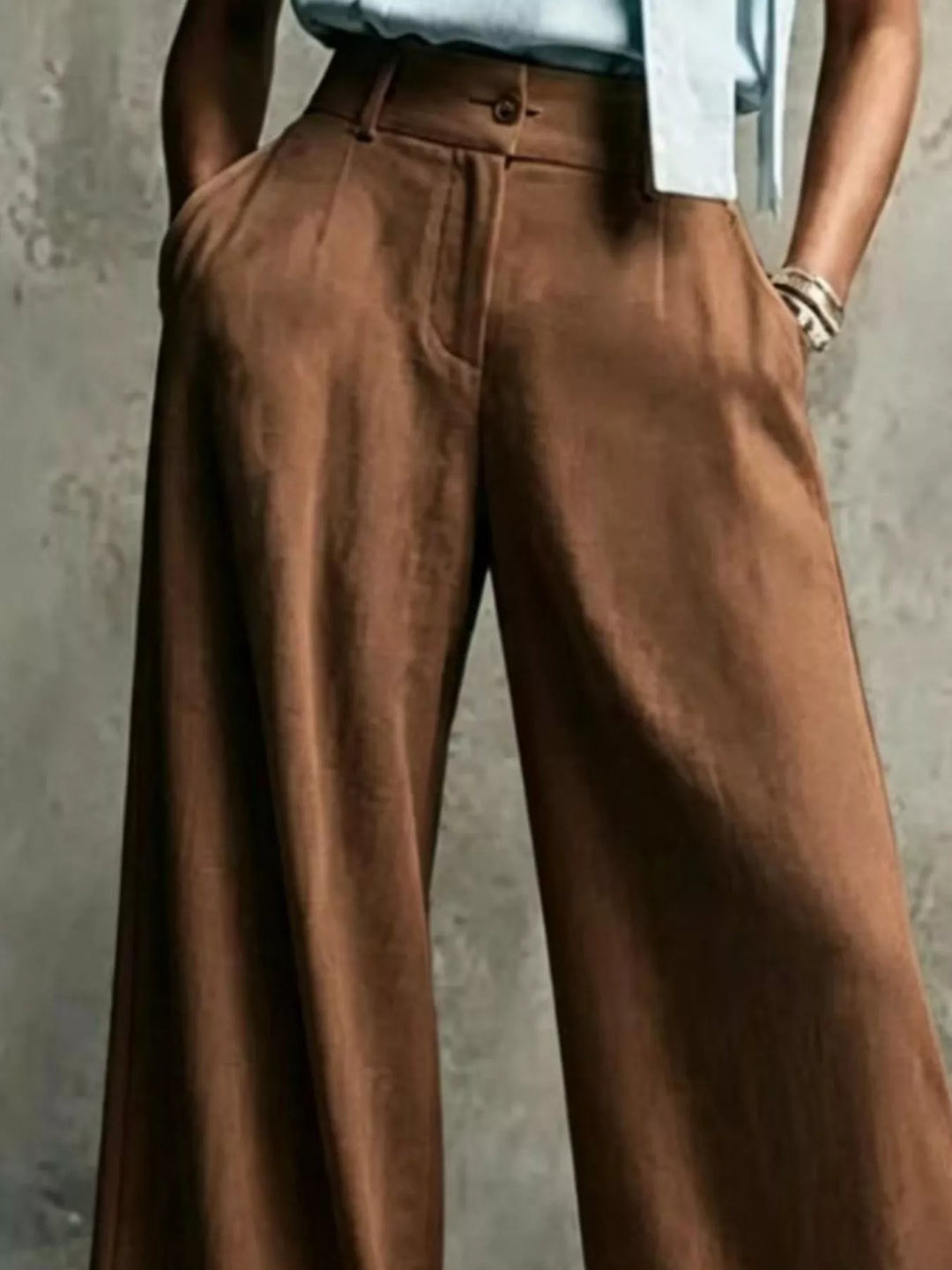 Brown pleated trousers, close-up showing the button and zip waistband
