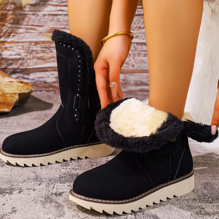 Black winter boot with the fur lined interior folded down, hand holding the cuff
