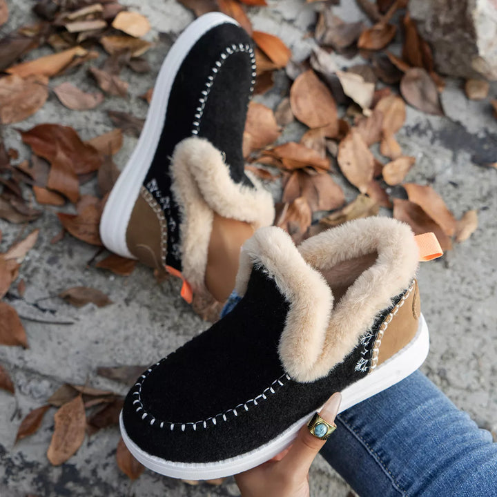 Black slip on boot held in hand showing the plush collar and stitched trim