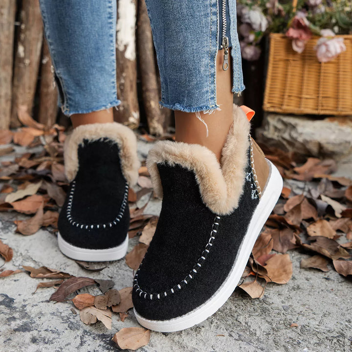Black slip on ankle boots with plush collar worn with jeans on leaves