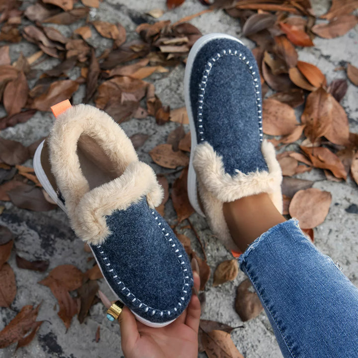 Denim blue winter boots held in hand showing the fluffy collar and heel tab