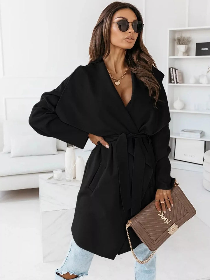 Black belted winter coat with hand on hip and a chain strap bag