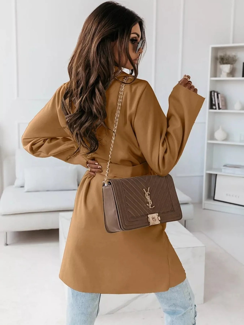 Camel belted coat with a quilted shoulder bag, over-the-shoulder pose