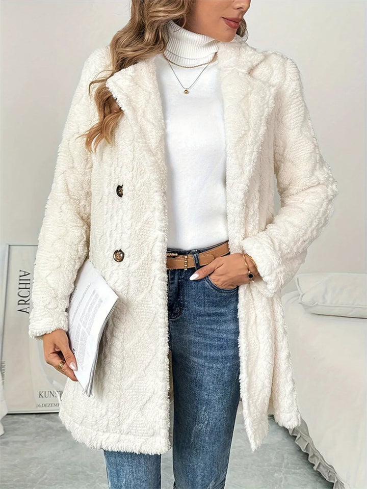 Ivory longline coat styled with jeans and a brown belt, holding papers